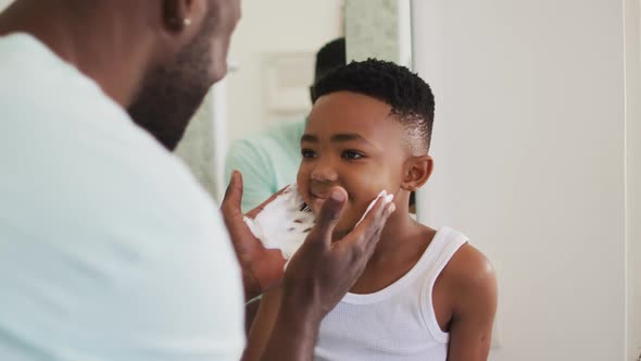 African american father putting shaving cream on his son mouth and laughing together alt