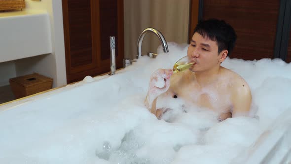 relaxed man drinking wine from glass while enjoying bubble bath in bathtub