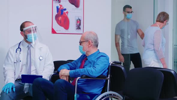 Doctor Consulting Disabled Senior Man in Hospital Waiting Area alt