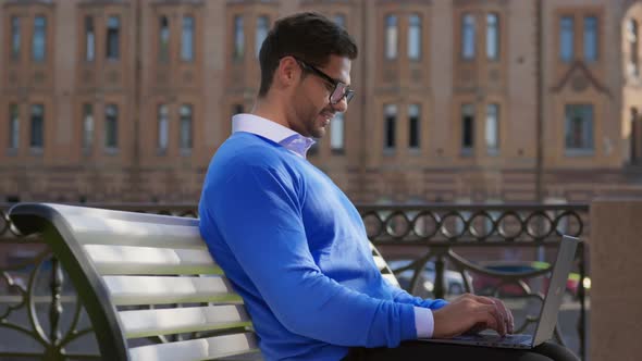 Pleased Indian Businessman Using Laptop While Sitting on Bench Outdoors alt
