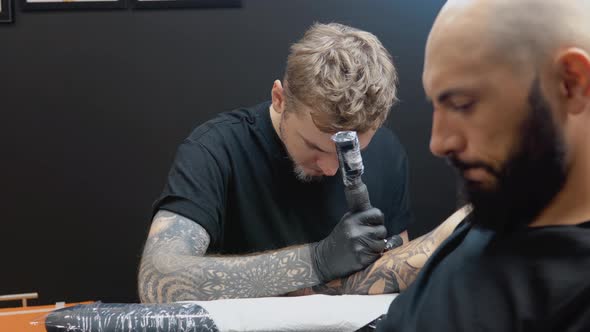 The Client Sits in a Chair While the Tattoo Artist Draws a Picture on His Hand Skin alt