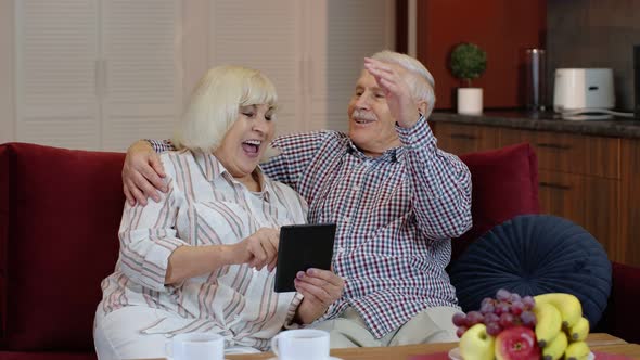 Senior Old Couple Grandparents Talking and Using Digital Tablet Computer at Home. Internet Shopping alt