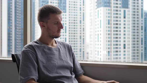 Exhausted Caucasian Office Man Working Late Looking Through the Window at the Concrete Jungle alt