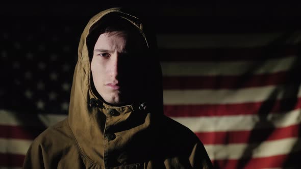 A Young Man in Uniform Stands Against the Background of the American Flag alt