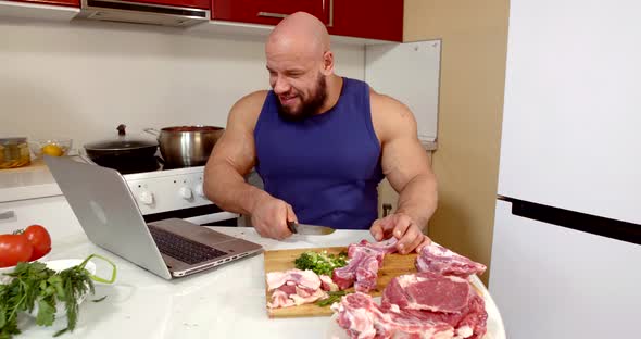 Brawny Man Is Slicing Meat and Watching Cinema on Laptop, Sitting at Kitchen Alone in Weekend alt