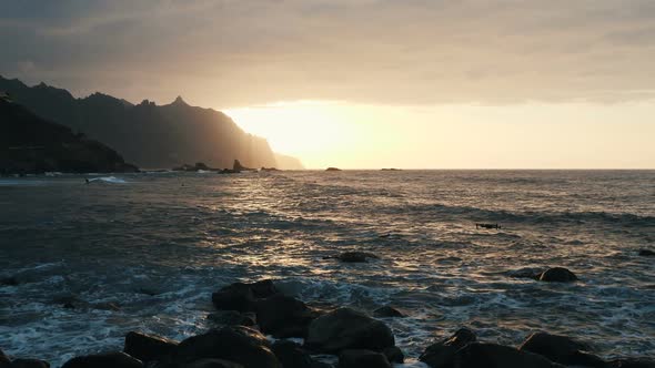 Drone Flies Over Ocean Waves Crashing on Rocks and Spraying in Beautiful Sunset Light at Benijo alt
