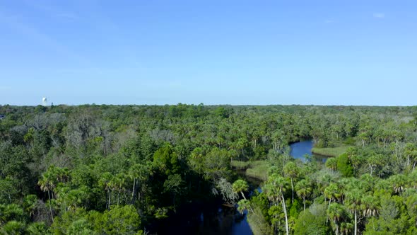 Rising Aerial of a River Flowing Through Forest and Towards a Suburban Town alt