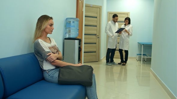 Female patient waiting in hospital hall while two doctors