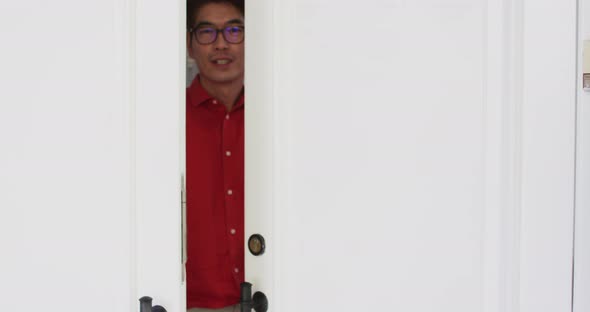 Happy asian man opening front door, smiling and greeting visitor to home alt