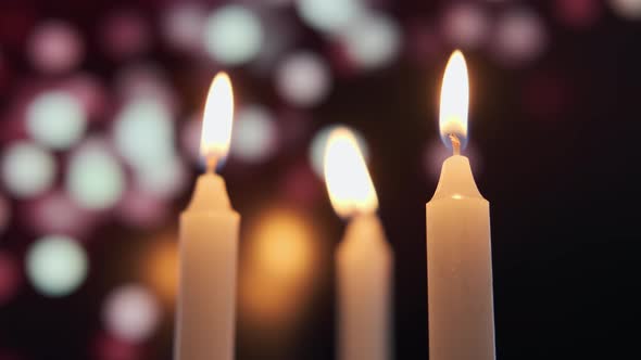 Footage of Burning a Three Candles on on a Background of Colored Blurred Bokeh alt