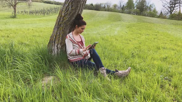 Woman using tablet, sitting on meadow alt