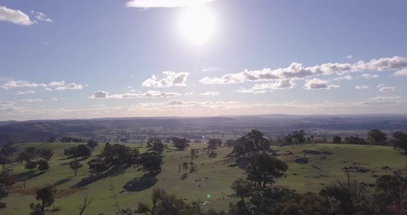 Aerial flight over forest in Australia with sun and clouds in the background, distance shot moving f alt