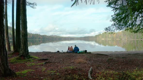 TRACKING shot of two adult women and a child sitting by a glassy lake in Sweden alt