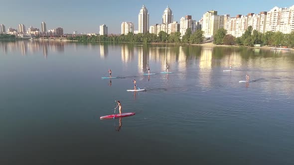 Flying Over a Group of People Exercising on a Sup Board on a River Against the Backdrop of the City