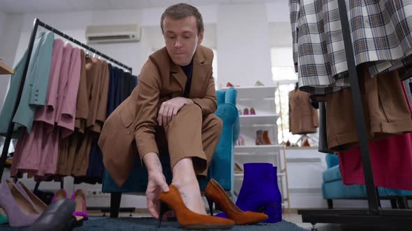 Wide Shot Thoughtful Confident Gay Man in Mustard Suit Trying on Dark Amber Highheels in Slow Motion alt