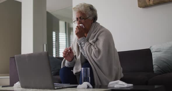 Sick african american senior woman coughing while having a video call on laptop at home alt