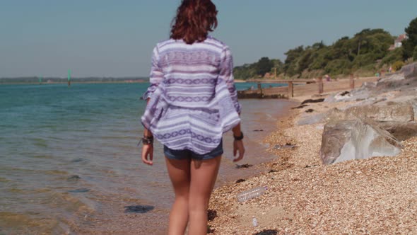 Young Woman Walks Along Beach and Picks Up Plastic Bottle alt