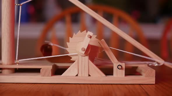 SLOW MOTION: Close up of a toy wooden trebuchet firing on a wooden table with a chair and counter in alt