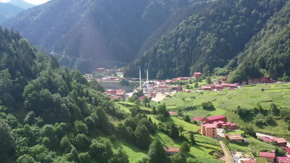 aerial drone flying over a large mountain forest hill revealing a beautiful lake and mosque in the v alt