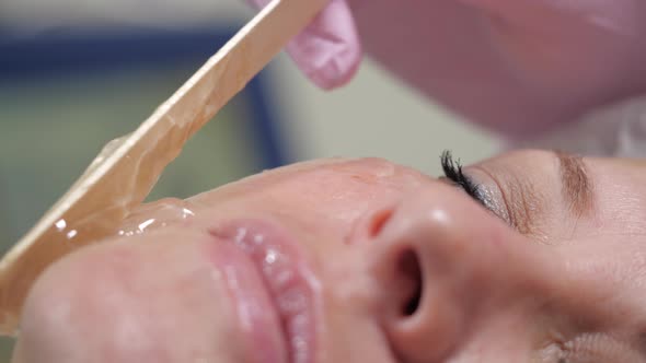 Applying a Transparent Gel on the Cheeks of a Woman with a Wooden Stick.