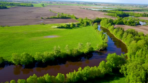 UHD aerial birds eye view of a small river flowing alongside some fields alt