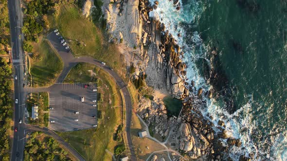 cars driving along coastal road near Maidens Cove Tidal Pool in Cape Town at sunset, aerial alt