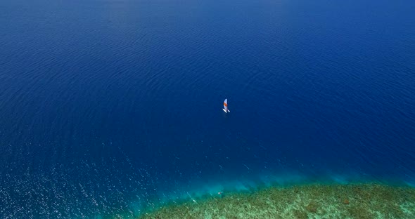 Aerial drone view of a man and woman sailing on a boat to a tropical island alt