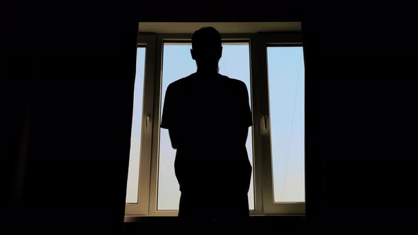 Silhouette of Man Opening Curtains and Looking Out of Window at Morning