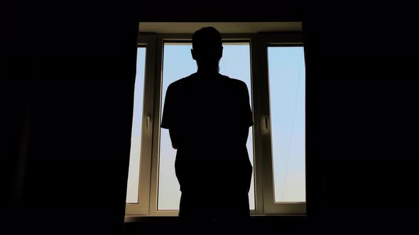 Silhouette of Man Opening Curtains and Looking Out of Window at Morning alt