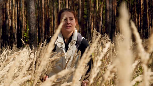 Slow Motion Video of Young Smiling Woman Walking in Forest and Moving Aside High Tall Grass alt