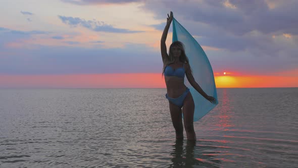 A Girl in a Blue Swimsuit and a Bright Pareo Posing Against the Background of a Sunset in Estuary alt