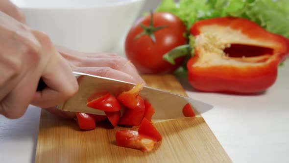 Confident Female Hands are Cutting Red Bell Pepper Into Cubes on a Wooden Cutting Board