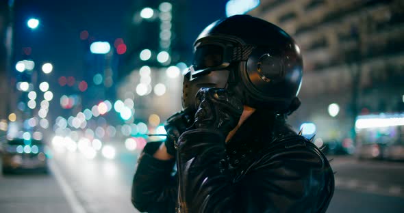 Motorcyclist Takes Off Black Helmet on City Road or Street at Night with Lights