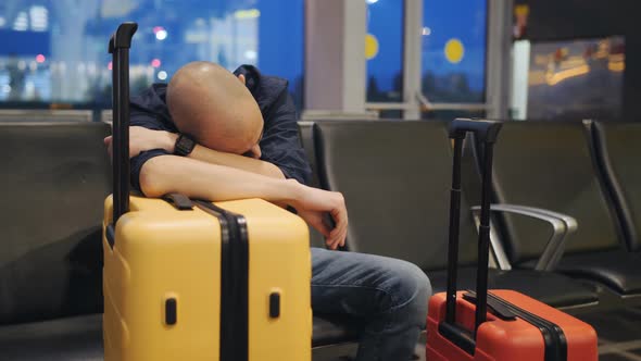 A Man Sleeping Leaning on the Yellow Suitcase in the Airport Lounge alt