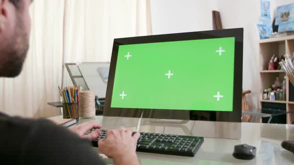 Young Artist Working at His Computer with Green Screen on the Display alt