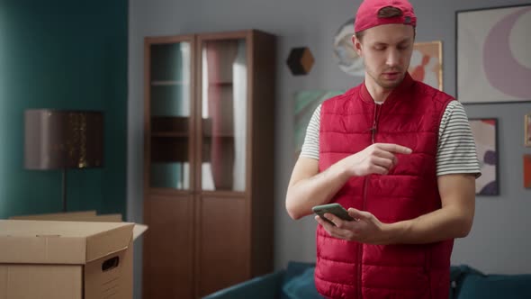 Delivery Man Counting Boxes in New Apartment and Writing Result in Smartphone alt
