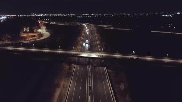 Aerial footage at night of a lighted highway with cars driving across bridges on all lanes