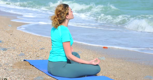 Young Woman Meditates on the Shore of the Ocean