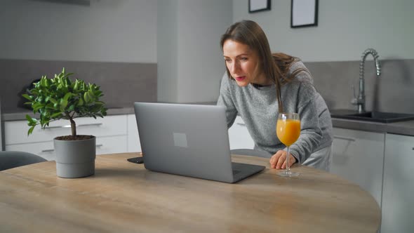 Woman Standing in Home Cozy Kitchen Leaning Over the Table and Communicates Via Video Link with alt