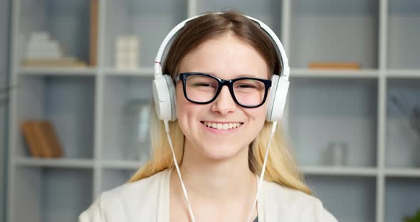 The face of a young female student in headphones greets with a hand on a web camera. 4K.