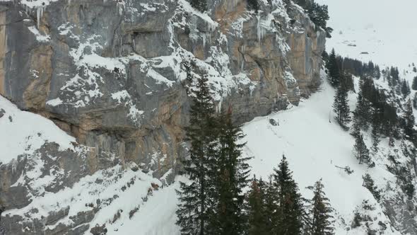 Aerial of hikers walking over mountain path, tilting up to frozen mountain wall alt