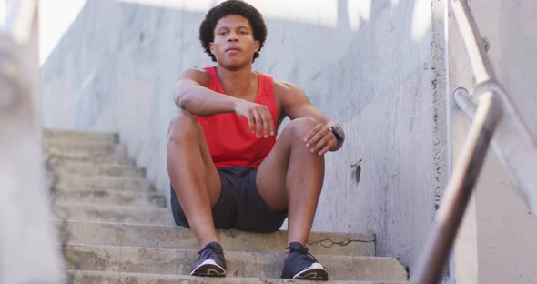 African american man exercising in city, sitting on steps and tying shoelaces alt