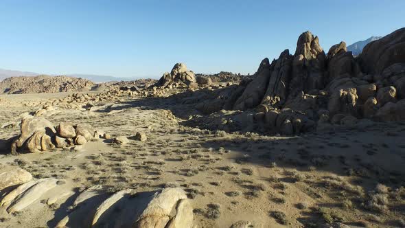 Aerial shot of a young man backpacker standing on a boulder with his dog in a desert mountain range. alt