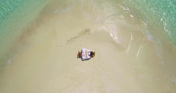 Aerial drone view of a man and woman eating breakfast on a tropical island sandbar beach alt