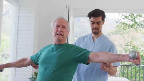 Young male physiotherapist helping retired senior man exercising with dumbbells at nursing home alt