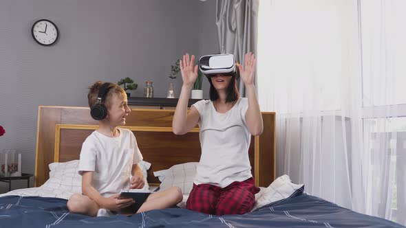 Small Boy Using Tablet PC while His Smiling Carefree Mother Using Virtual Reality Headset at Home alt