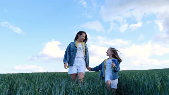 Mom and Daughter Walk in a Green Field of Young Wheat alt