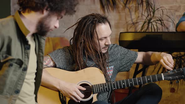 Young Music Band Preparing for Performance on Stage Man Guitarist with Dreadlocks Tuning His Guitar alt