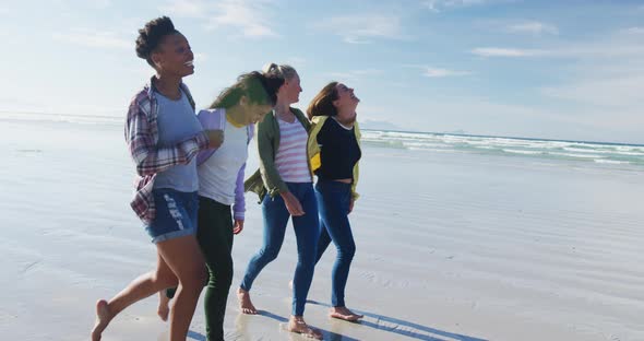 Happy group of diverse female friends having fun, walking along beach alt
