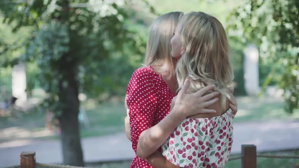 Two Attractive Blonde Girlfriends Talking and Hugging in the Park alt